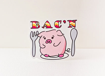 Cartoon pig holding utensils with 'BAC'N' text on a white background